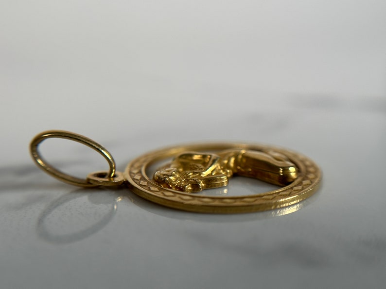 May include: A gold pendant with a detailed design of a woman's figure in a circle. The pendant has a loop for attaching to a chain.