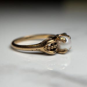 Puede incluir: Un anillo de oro con una perla engastada en una garra. El anillo es simple y elegante.