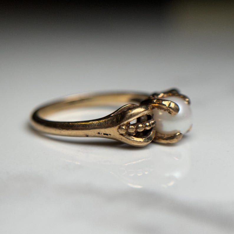 Puede incluir: Un anillo de oro con una perla engastada en una garra. El anillo es simple y elegante.