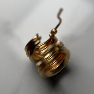 May include: Gold hoop earrings with a layered design. The earrings are open and ready to be worn.