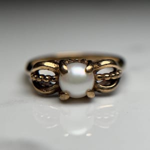 Puede incluir: Un anillo de oro con un dise&ntilde;o delicado que presenta una sola perla blanca en el centro.