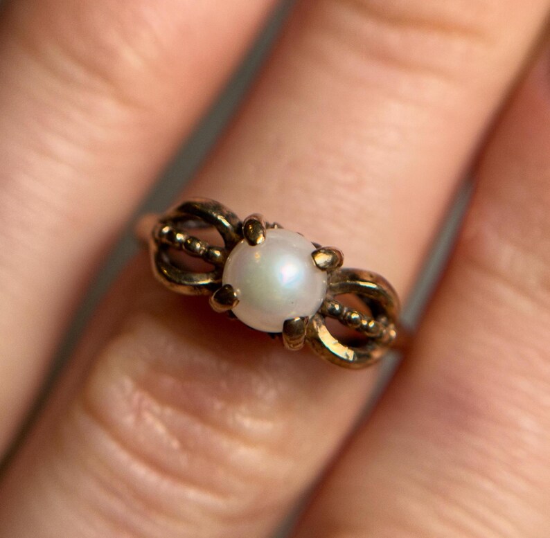 Puede incluir: Un anillo de oro con una perla blanca engastada en un dise&ntilde;o delicado y ornamentado.