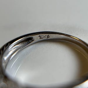 May include: Close-up of the inside of a silver ring with the inscription "10KS" on the band.