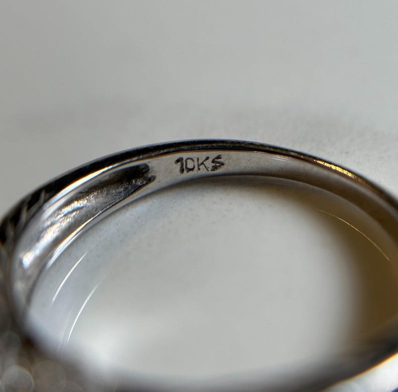May include: Close-up of the inside of a silver ring with the inscription "10KS" on the band.