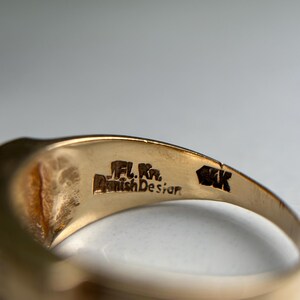 May include: Close-up of a gold ring with the text "JFL. Kr. Danish Design" and "14K" engraved on the inside. The ring has a smooth, polished surface and a classic design.