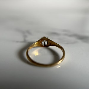 May include: A gold ring with a single clear stone set in the center. The ring is simple and elegant.