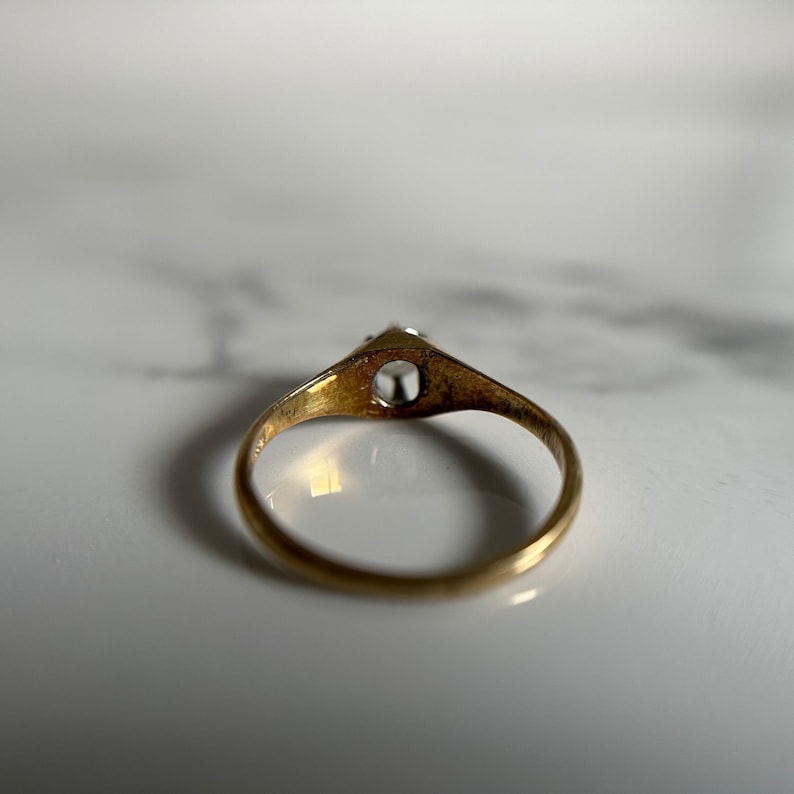 May include: A gold ring with a single clear stone set in the center. The ring is simple and elegant.