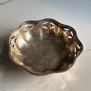 May include: A silver bowl with a scalloped edge and a cut-out design of leaves and flowers.