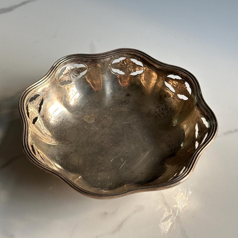 May include: A silver bowl with a scalloped edge and a cut-out design of leaves and flowers.