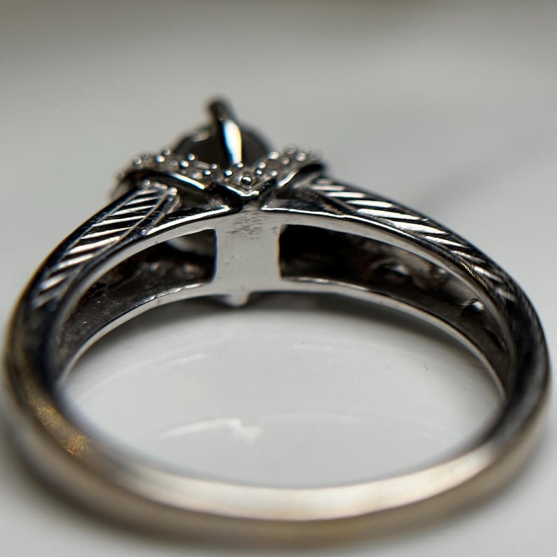 May include: A silver ring with a diamond set in a prong setting. The ring has a textured band and a decorative design on the top.