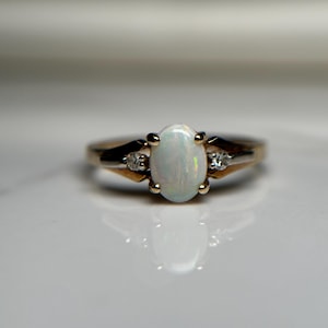 Peut inclure: Une bague en or avec une pierre centrale en opale ovale et deux petits diamants d'accent. L'opale est d'un blanc laiteux pâle. La monture de la bague est en or, avec un design classique et élégant.