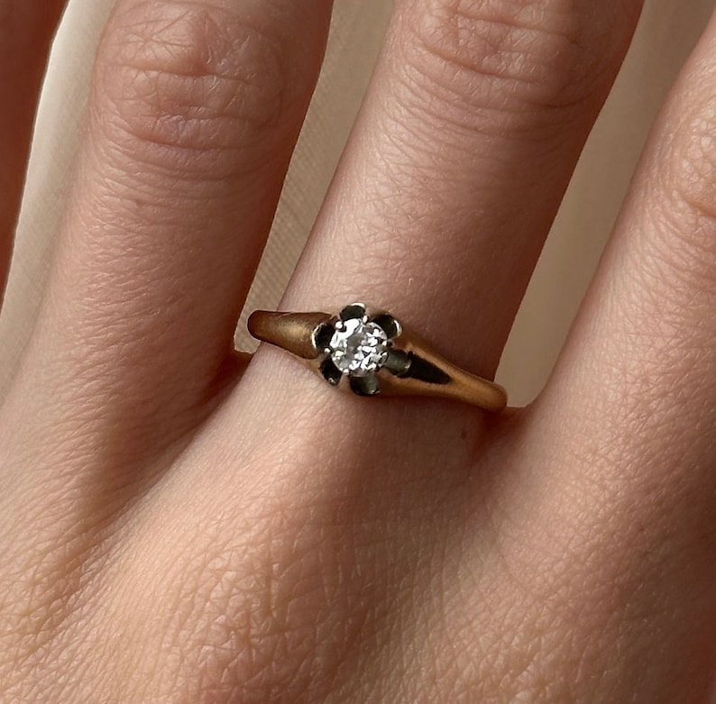 May include: A gold ring with a single round diamond set in a flower-shaped setting.