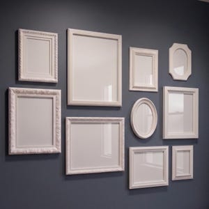 May include: A collection of nine white picture frames of varying sizes and shapes, including rectangular and oval designs, arranged on a dark gray wall. The frames feature diverse border styles, ranging from smooth edges to ornate, decorative carvings.