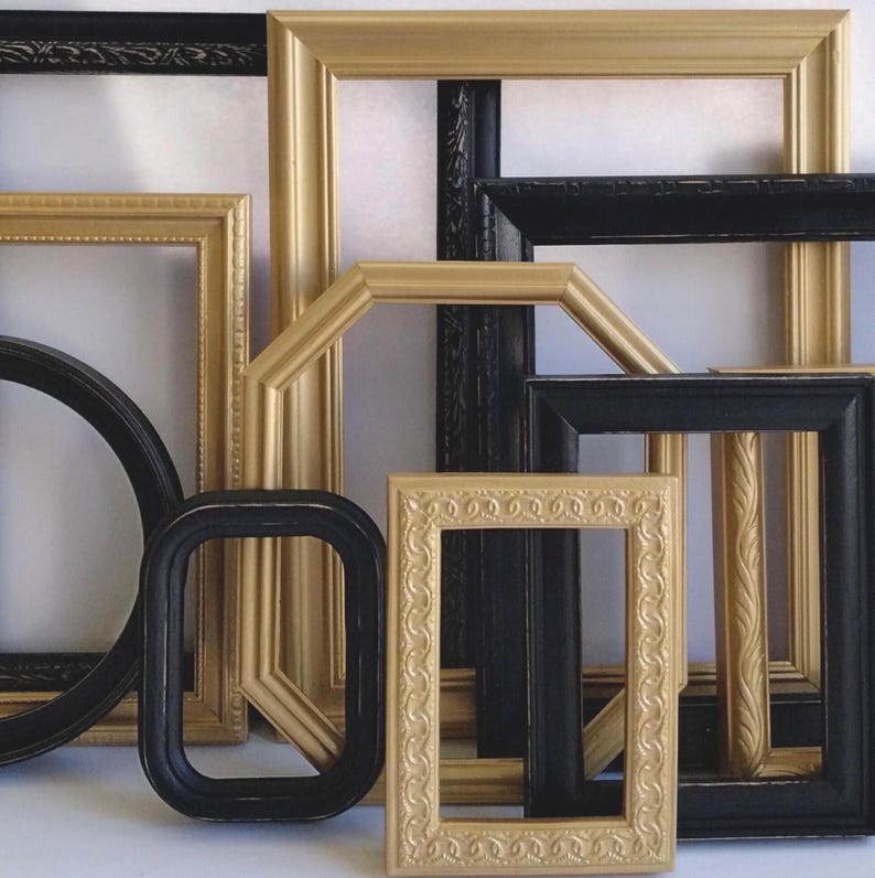 Gallery wall collection of assorted vintage picture frames in various sizes, styles, shapes. Many of the frames have ornate designs and details. The frames are painted black and gold. Some frames have ornate designs, while others are more simple.