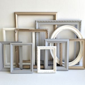 May include: A collection of various empty picture frames in shades of white, gray, and gold. The frames are in different shapes and sizes, including rectangular and oval. Some frames have ornate detailing.