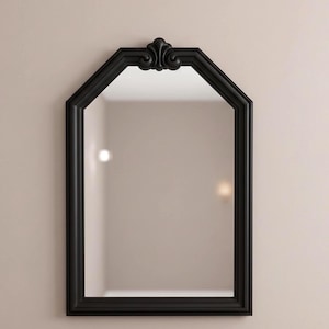 May include: Black framed wall mirror with an arched top and decorative scrollwork. The mirror has a rectangular shape with a beveled edge and is mounted on a neutral-colored wall. The mirror's frame has a matte finish.