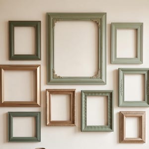 May include: A collection of nine empty picture frames arranged on a wall. The frames vary in size and rectangular shape, featuring a mix of sage green and metallic bronze finishes. Some frames have smooth edges, while others display ornate corner details.
