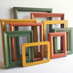May include: A collection of rectangular picture frames in various sizes and colors, including shades of olive green, mustard yellow, and terracotta orange. The frames feature diverse border textures, such as beaded, smooth, and wavy edges.