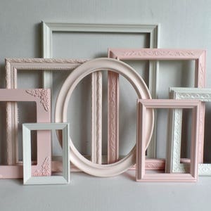 May include: A set of eight white and pink picture frames with ornate detailing. The frames are arranged in a staggered pattern, with the largest frame at the top and the smallest frame at the bottom.