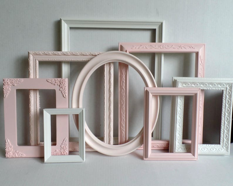 A gallery wall set of assorted vintage picture frames painted rose pink, blush and white. Many frames have ornate details while others are more simple styles. Picture frames are various sizes, shapes and styles. The frames have a elegant antique look.