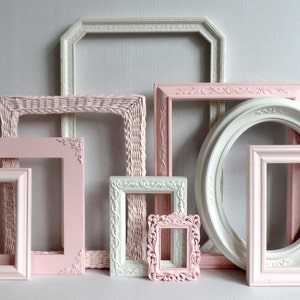 A gallery wall collection of assorted vintage picture frames rose pink, blush  and white. Many frames have ornate details while others are more simple styles. Picture frames are various sizes, shapes and styles. The frames have a elegant antique look.