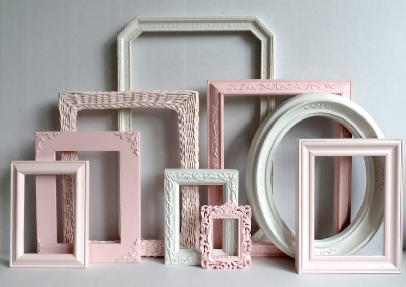A gallery wall collection of assorted vintage picture frames rose pink, blush  and white. Many frames have ornate details while others are more simple styles. Picture frames are various sizes, shapes and styles. The frames have a elegant antique look.