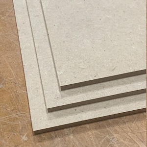 May include: Three pieces of beige particle board stacked on top of each other. The boards are rectangular and have a rough texture.