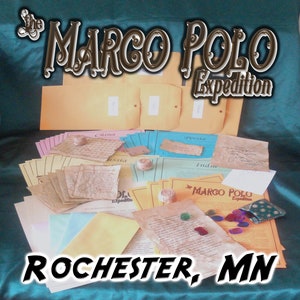 May include: A display of aged paper documents, maps, and envelopes, with the text "The Marco Polo Expedition" and "Rochester, MN". The items are arranged on a teal surface, suggesting a historical or educational theme.