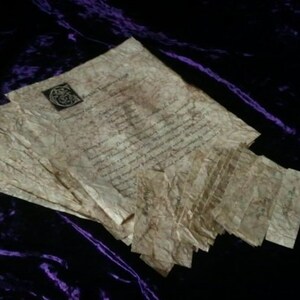 May include: A stack of aged parchment papers with handwritten text and a decorative emblem. The papers have a crinkled texture and a sepia tone, suggesting an antique or vintage aesthetic. The background is a dark purple velvet.
