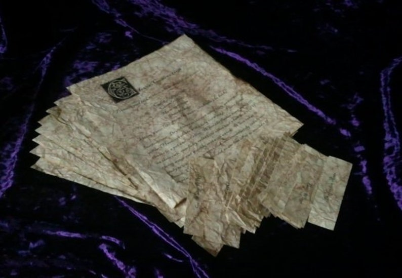 May include: A stack of aged parchment papers with handwritten text and a decorative emblem. The papers have a crinkled texture and a sepia tone, suggesting an antique or vintage aesthetic. The background is a dark purple velvet.