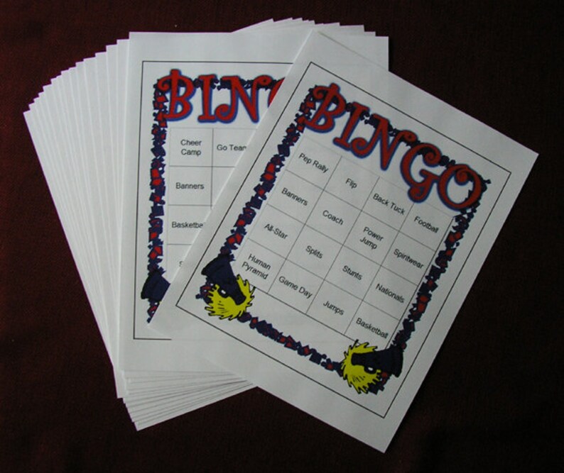 May include: A stack of white Bingo cards with red and blue decorative borders. The word "BINGO" is in large red letters at the top. Each card has a grid of squares with words like "Cheer Camp", "Banners", and "Basketball".