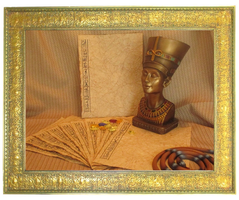 May include: A framed display featuring an Egyptian theme. It includes a bust of Nefertiti, papyrus scrolls with hieroglyphs, and a coiled snake. The frame is gold-colored with intricate detailing, and the background is a textured tan fabric.
