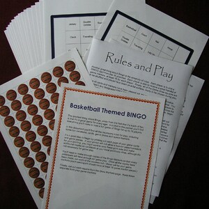 May include: A stack of printed basketball-themed Bingo game materials. Includes rules, game cards, and sheets of basketball-shaped markers. The text on the pages reads "Basketball Themed BINGO" and "Rules and Play".