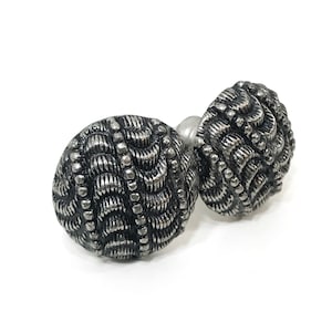 May include: Two silver-toned cabinet knobs with a textured, woven design. The knobs are round and have a slightly raised edge.