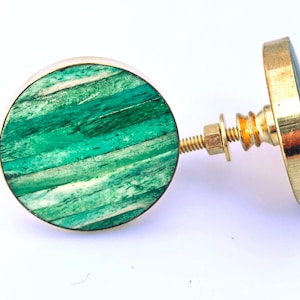 May include: Two decorative cabinet knobs. Each knob features a round, green and white striped face with a gold-colored metal rim. The knobs have a gold-colored metal base and screw for attachment.