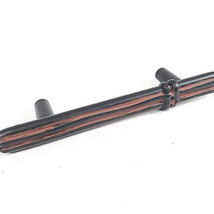 May include: Black cabinet pull with a brown woodgrain design. The pull has a rectangular shape with rounded edges and a knot detail in the center.