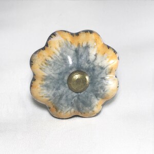May include: A ceramic flower-shaped knob with a gray and yellow glaze. The knob has a brass center.