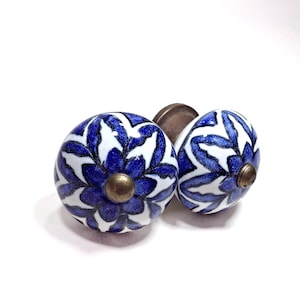 May include: Two ceramic cabinet knobs with a blue and white floral design. The knobs have a round shape with a brass-colored base. The floral pattern is a stylized, repeating design.