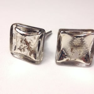 May include: Two square-shaped glass cabinet knobs with a silver finish. The knobs have a slightly raised, diamond-shaped design in the center.