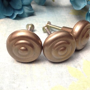 May include: Four gold-toned metal cabinet knobs with a spiral design. The knobs have a brushed finish and are attached to screws.