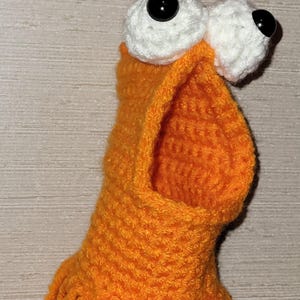 May include: A handmade orange crochet monster with large white eyes and black pupils. The monster has a wide open mouth and fringe at the bottom. It is hanging from a horseshoe.