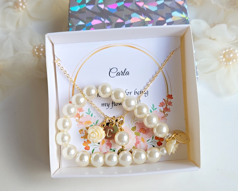 K&ouml;nnte beinhalten: Eine wei&szlig;e Geschenkbox mit einem goldenen Perlen-Halsketten- und Armband-Set. Die Box enth&auml;lt eine Karte mit der Aufschrift "Carla, daf&uuml;r, dass du meine Blume bist".