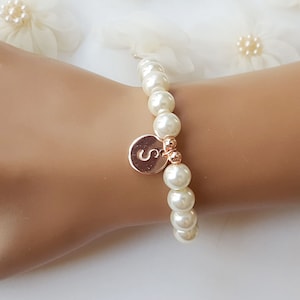 May include: A white pearl bracelet with a gold charm featuring the letter 'S'.