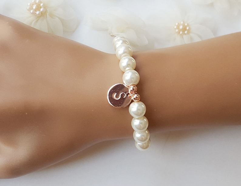 May include: A white pearl bracelet with a gold charm featuring the letter 'S'.