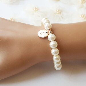 May include: A white pearl bracelet with a gold initial charm. The initial is the letter "S".