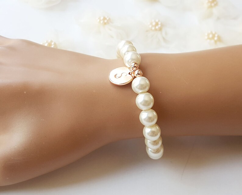 May include: A white pearl bracelet with a gold initial charm. The initial is the letter "S".