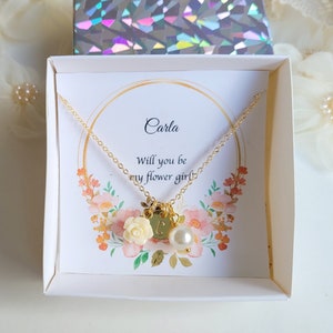 K&ouml;nnte beinhalten: Eine wei&szlig;e Schachtel mit einer goldenen Halskette darin. Die Halskette hat einen kleinen Blumenanh&auml;nger und einen Perlenanh&auml;nger. Die Schachtel hat eine Karte mit der Aufschrift "Carla, Willst du meine Blumenm&auml;dchen sein?"