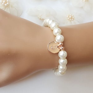 May include: A white pearl bracelet with a gold charm featuring the letter 'S'.
