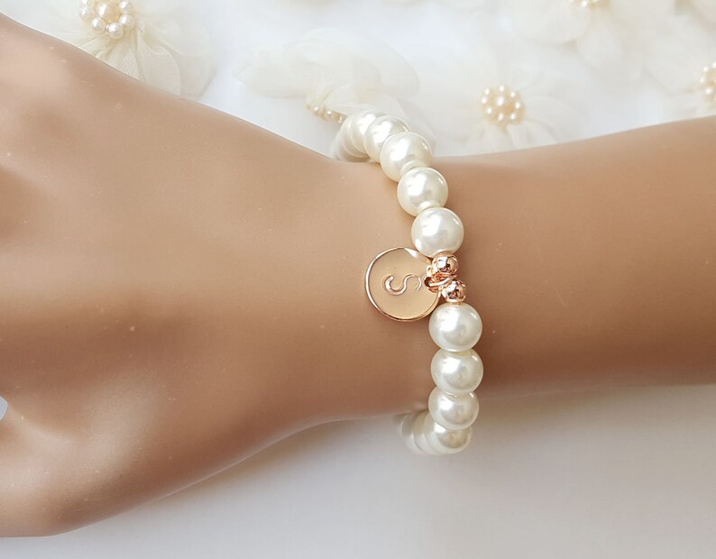 May include: A white pearl bracelet with a gold charm featuring the letter 'S'.