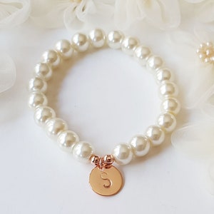 May include: A white pearl bracelet with a gold charm featuring the letter 'S'.